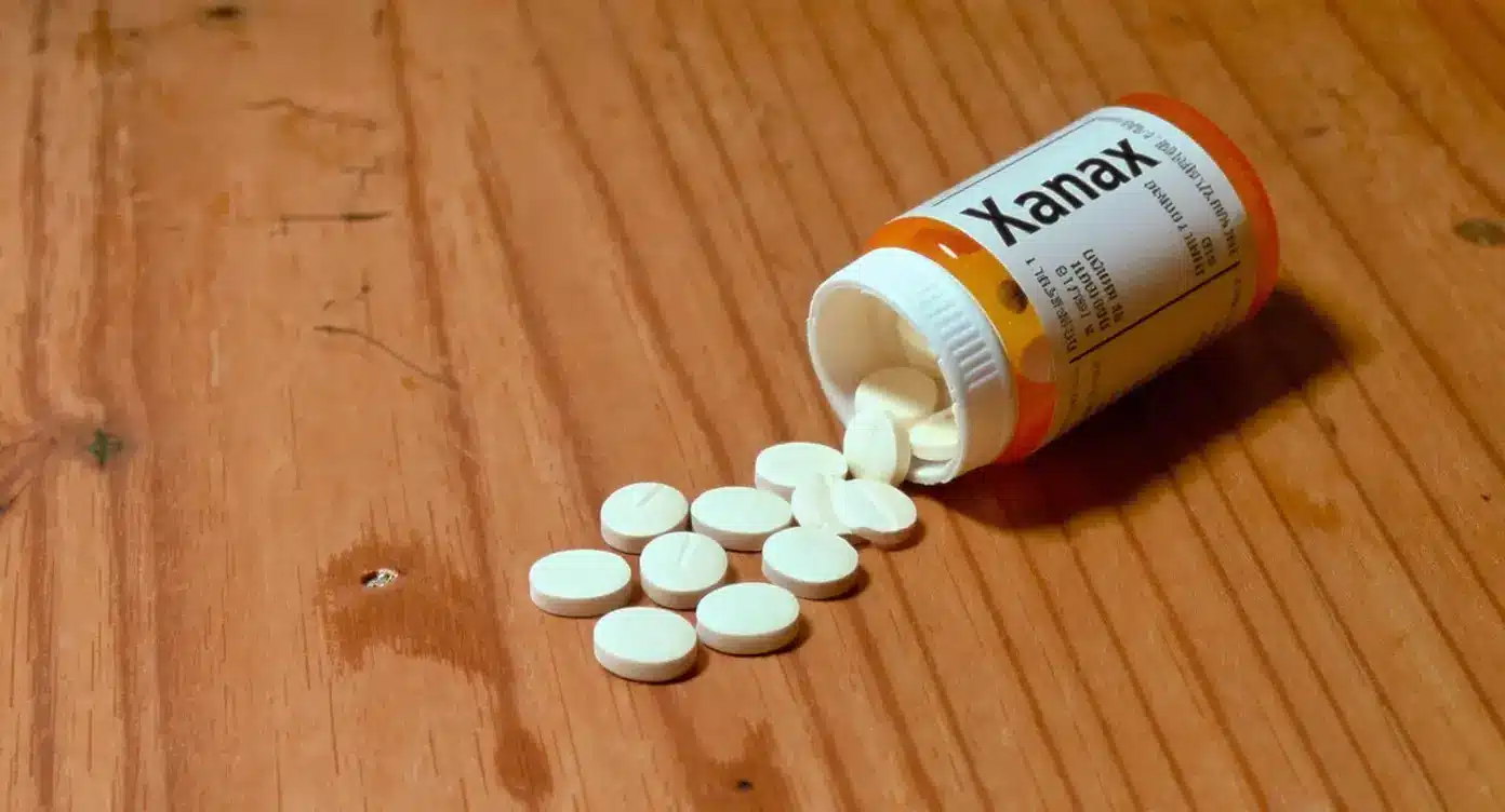 Prescription Xanax bottle tipped over with tranquilizer tablets on wooden surface