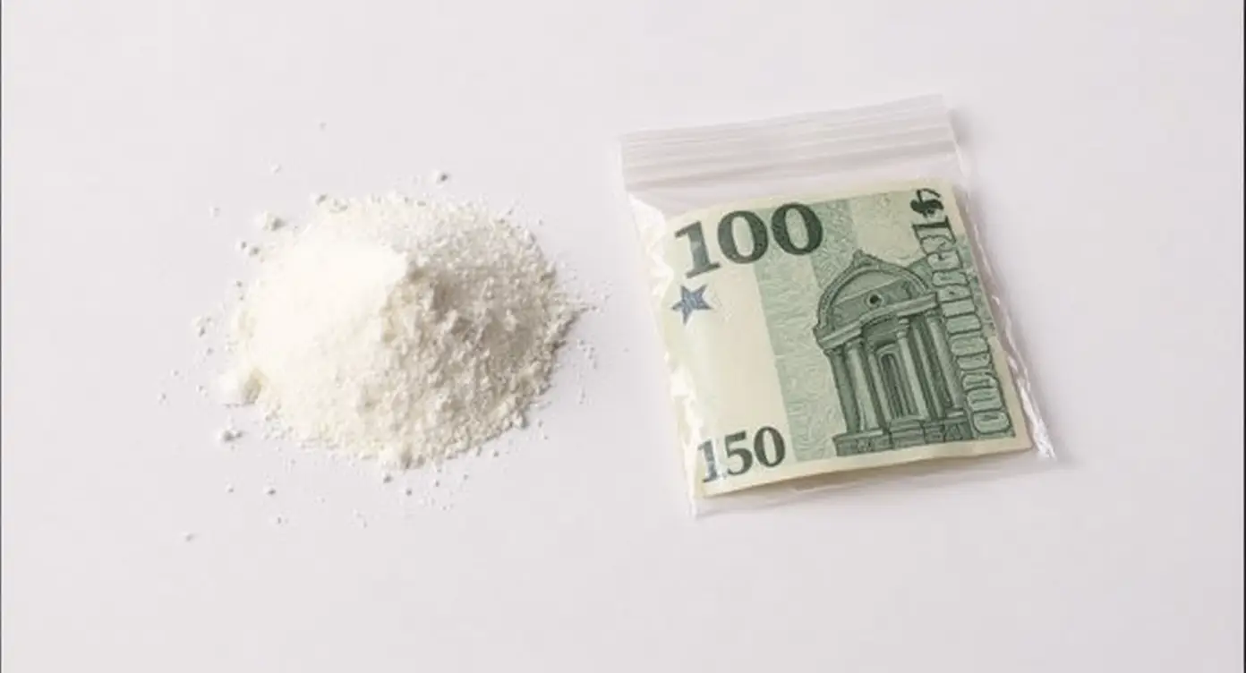 Pudră albă de cocaină lângă bancnotă euro și pungă de plastic pe fundal alb